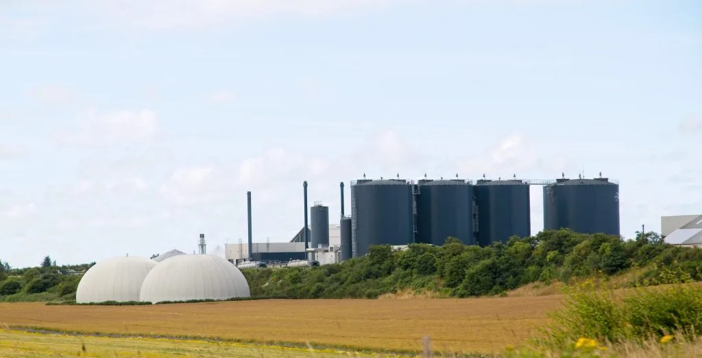 Biogasanlage mit weißen Fermenterkuppeln vor einer größeren Industrieanlage